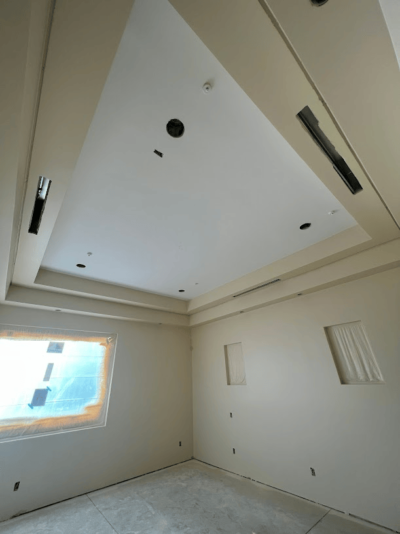 Unfinished room with recessed ceiling and wall niches, window covered for protection.