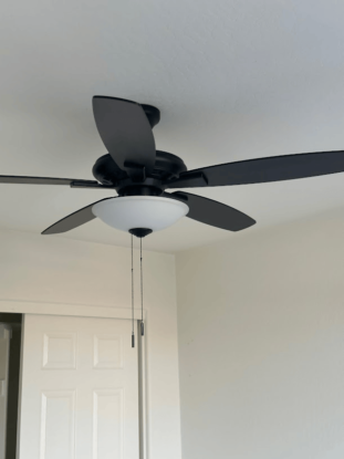 Black ceiling fan with light fixture and pull chains in a white room.