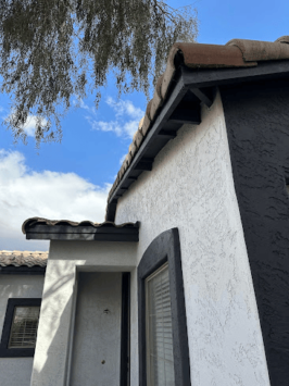 House exterior with white and dark gray stucco walls and a tiled roof under a partly cloudy sky.
