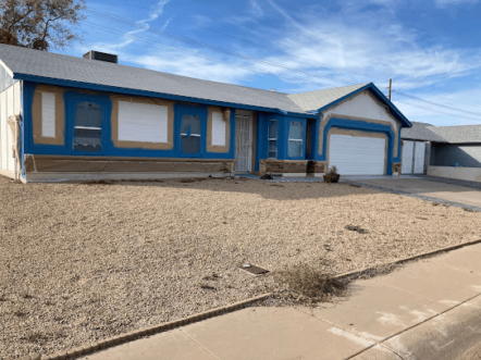 House exterior in painting prep with taped edges; yard has gravel and some weeds.
