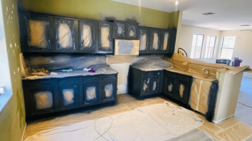 Kitchen cabinets being sprayed with dark paint, covered in protective plastic and paper