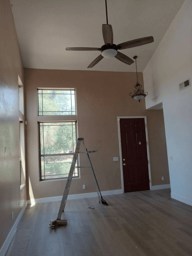 Room with ceiling fan, ladder, large windows, and red door.
