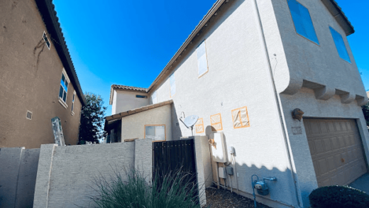 Two-story house exterior with gated side yard and clear blue sky.