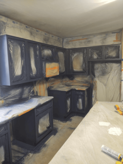 Kitchen under renovation with cabinets covered and spray-painted dark