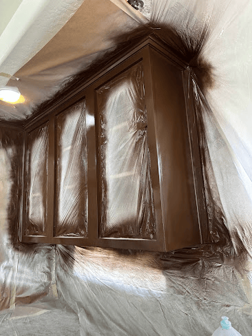 Kitchen under renovation with cabinets covered and spray-painted dark