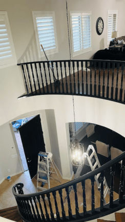 Curved staircase with black railing in a tall entryway, renovation in progress.