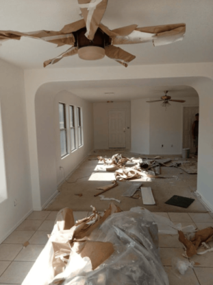 Living room under renovation with ceiling fans and debris on the floor.