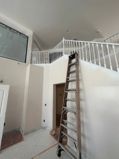 Indoor staircase area with a tall wooden ladder leaning against the wall.