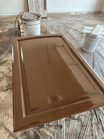 Wooden door being painted brown, with paint cans nearby